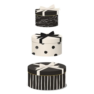Three stacked round gift boxes with black and white patterns, including stripes, polka dots, and abstract scribbles, each tied with a ribbon bow, on a white background.
