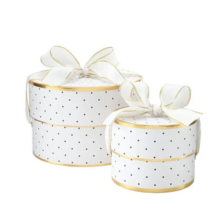 Two round white gift boxes with black polka dots, gold trim, and white ribbon bows on a plain white background.