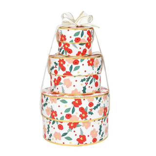 A stack of four round gift boxes in descending sizes, decorated with a red, pink, and green floral pattern and accented with gold trim, tied together with a sheer ribbon at the top.