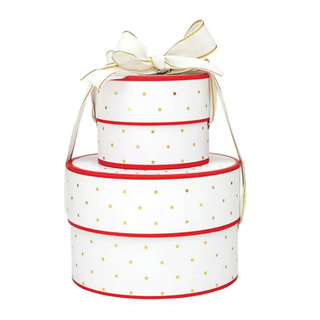A three-tier round gift box set in white with gold polka dots, accented by red trim and a cream-colored satin bow with gold detailing on top, set against a plain white background.